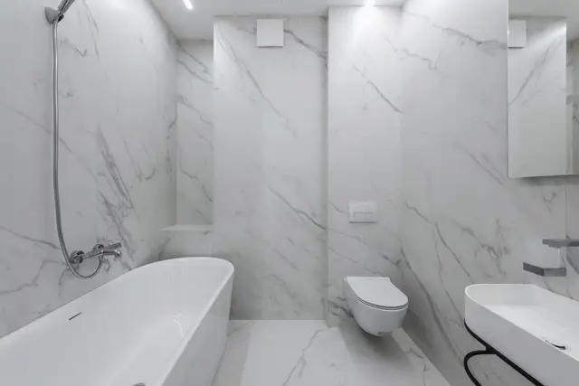 Bright marble bathroom with a tub and wall-hung toilet