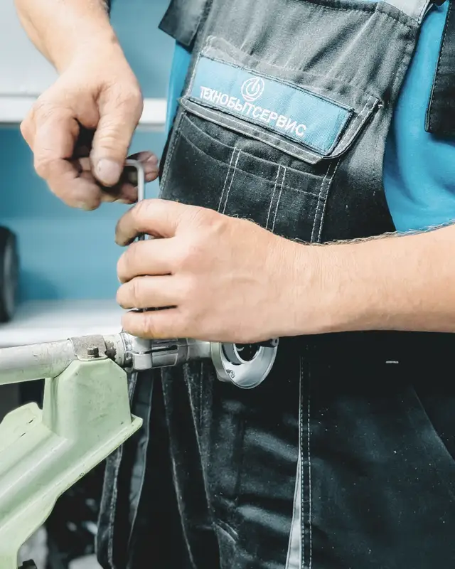 A plumber in a blue uniform working a wrench on a pipe fitting
